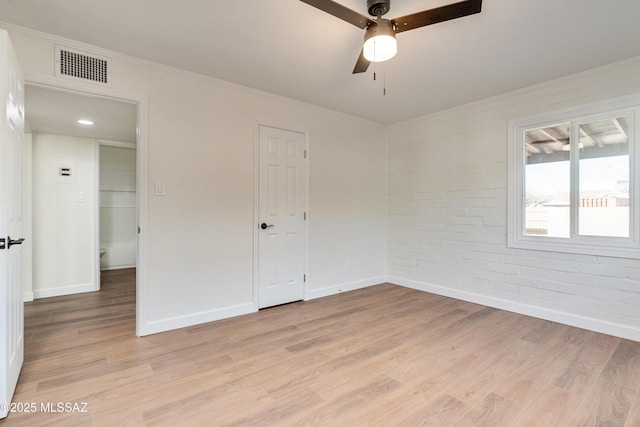 spare room featuring crown molding, visible vents, light wood-style floors, brick wall, and baseboards