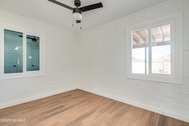 spare room with brick wall, ornamental molding, wood finished floors, and baseboards