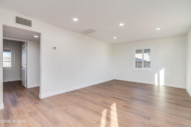 spare room featuring a healthy amount of sunlight, brick wall, visible vents, and wood finished floors