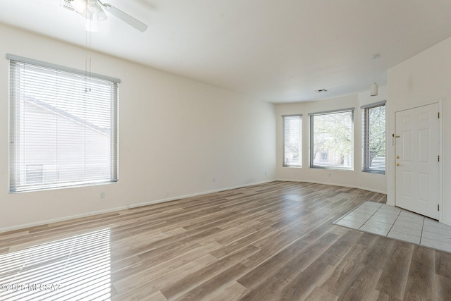 empty room with light wood-type flooring, ceiling fan, visible vents, and baseboards