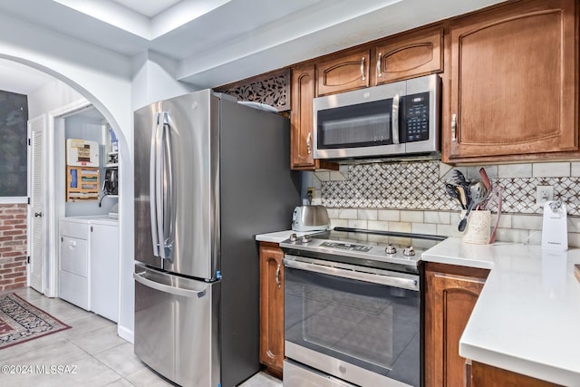 kitchen with light countertops, decorative backsplash, appliances with stainless steel finishes, brown cabinetry, and separate washer and dryer