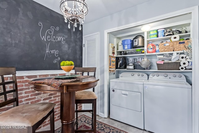 clothes washing area featuring washer and dryer, laundry area, light tile patterned flooring, and an inviting chandelier