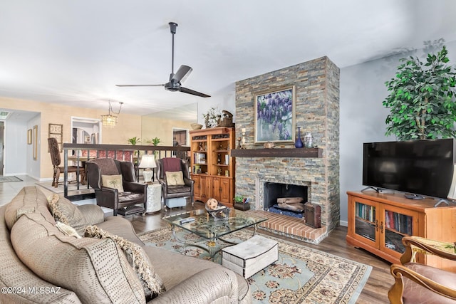 living room featuring a ceiling fan, a stone fireplace, baseboards, and wood finished floors