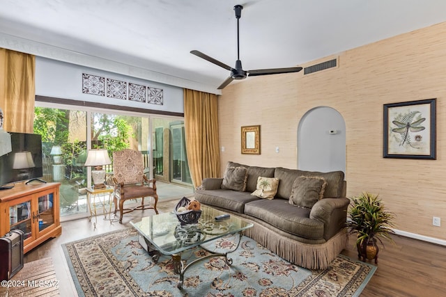 living area featuring arched walkways, wood finished floors, a ceiling fan, visible vents, and baseboards