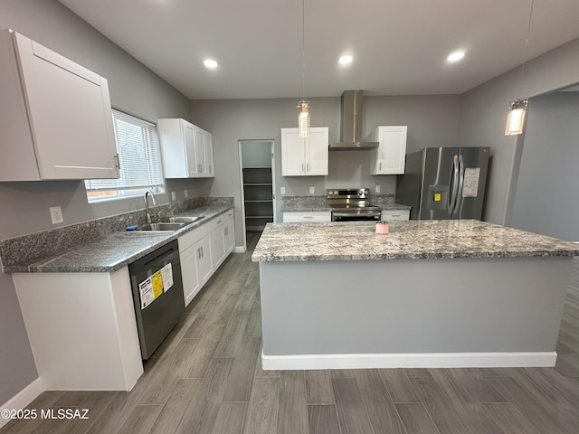 kitchen with a kitchen island, a sink, white cabinets, appliances with stainless steel finishes, and wall chimney exhaust hood