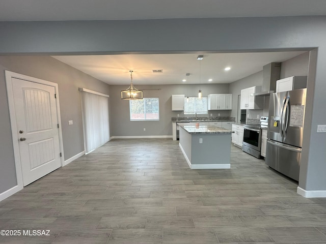 kitchen featuring white cabinets, wall chimney exhaust hood, appliances with stainless steel finishes, a center island, and hanging light fixtures