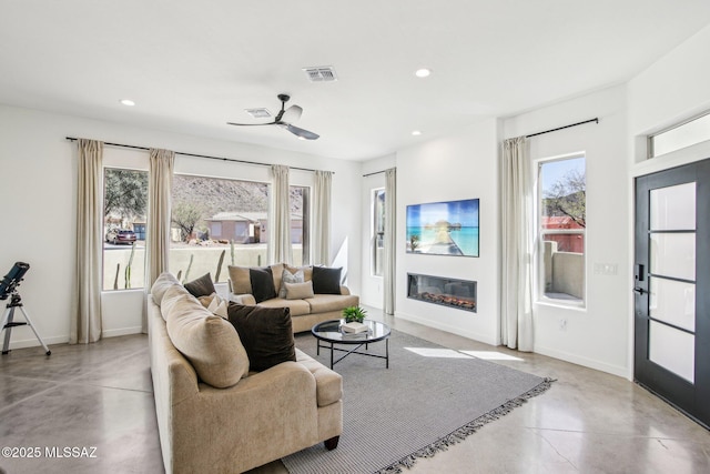 living area featuring concrete flooring, recessed lighting, visible vents, baseboards, and a glass covered fireplace