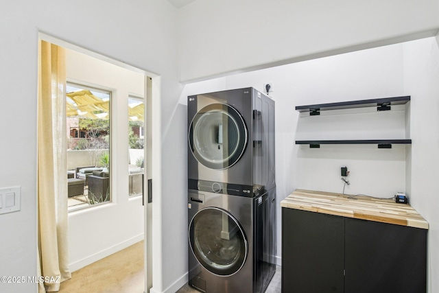 clothes washing area featuring light carpet, stacked washer and dryer, laundry area, and baseboards