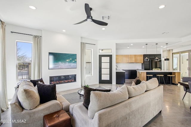 living area featuring recessed lighting, a glass covered fireplace, visible vents, and a healthy amount of sunlight