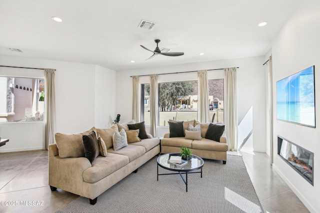 living area featuring plenty of natural light, visible vents, a glass covered fireplace, and recessed lighting