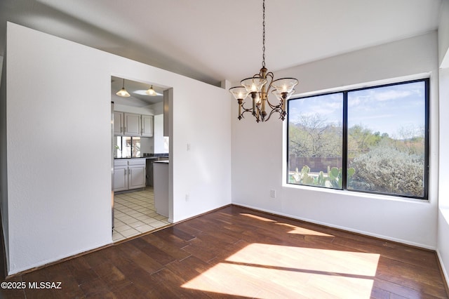 unfurnished dining area featuring baseboards, wood finished floors, and an inviting chandelier