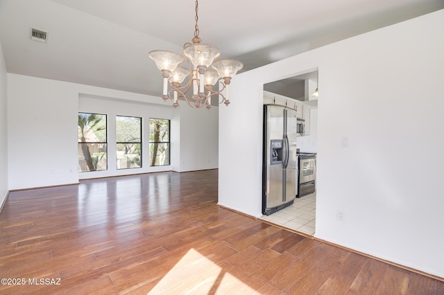 spare room featuring light wood-style flooring, visible vents, and a chandelier