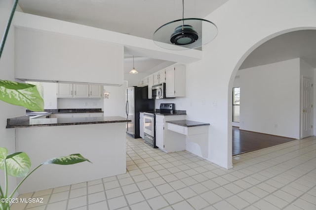 kitchen featuring arched walkways, white cabinets, dark countertops, a peninsula, and stainless steel appliances