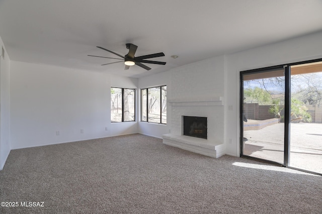 unfurnished living room with ceiling fan, a fireplace, carpet flooring, and a wealth of natural light