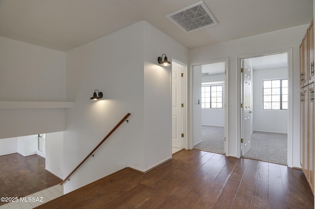 hallway with dark wood finished floors, an upstairs landing, visible vents, and baseboards