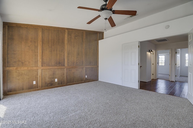 empty room with dark colored carpet, visible vents, and ceiling fan