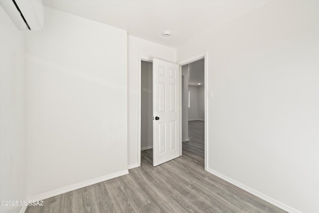 unfurnished bedroom with baseboards, wood finished floors, and a wall mounted AC