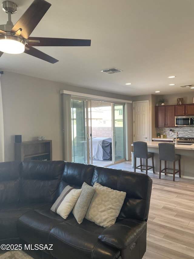 living area featuring light wood-type flooring, ceiling fan, visible vents, and recessed lighting