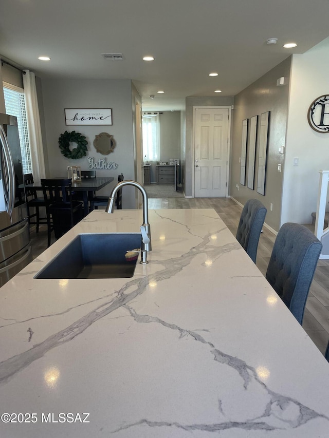 kitchen with recessed lighting, a sink, visible vents, stainless steel refrigerator with ice dispenser, and light stone countertops