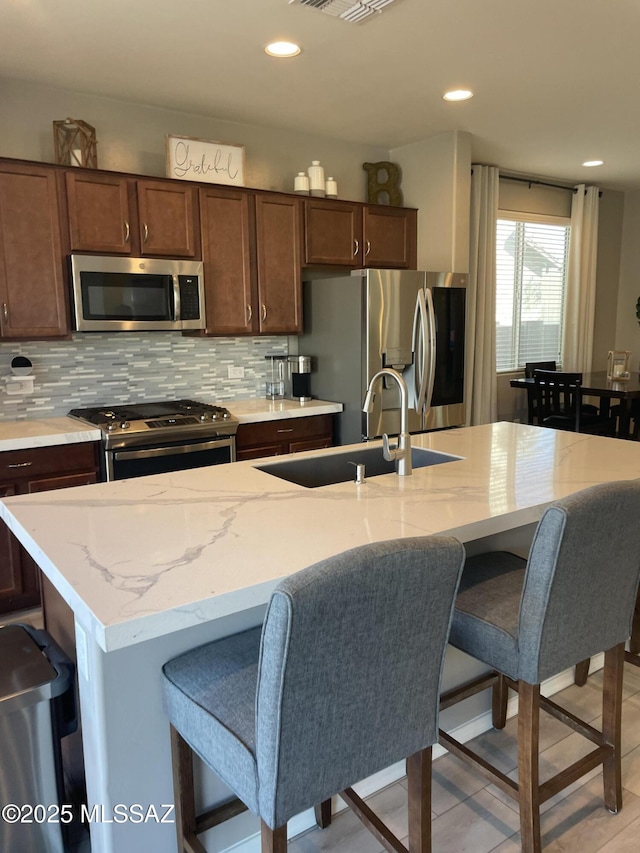 kitchen with appliances with stainless steel finishes, a sink, a breakfast bar area, and tasteful backsplash