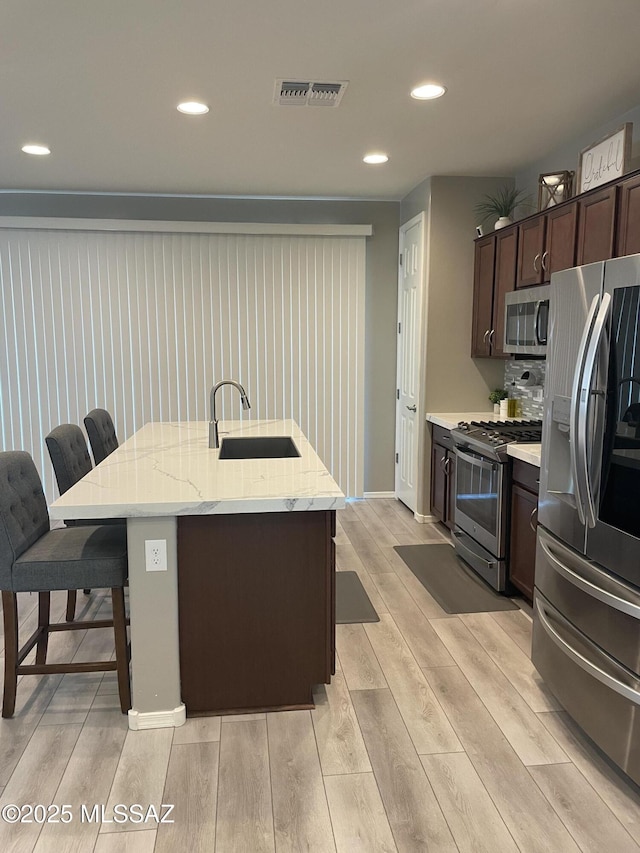 kitchen featuring a breakfast bar, wood finish floors, a sink, visible vents, and appliances with stainless steel finishes