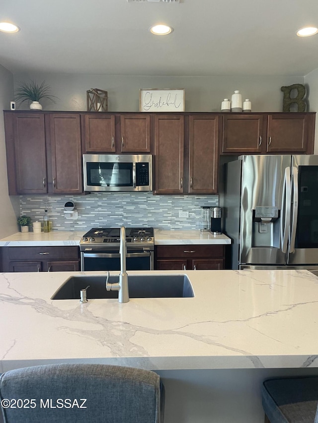 kitchen featuring light stone countertops, dark brown cabinets, stainless steel appliances, and decorative backsplash