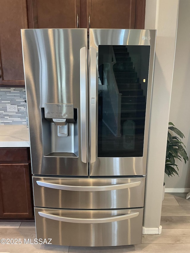 interior details with tasteful backsplash, baseboards, stainless steel fridge with ice dispenser, and wood finished floors