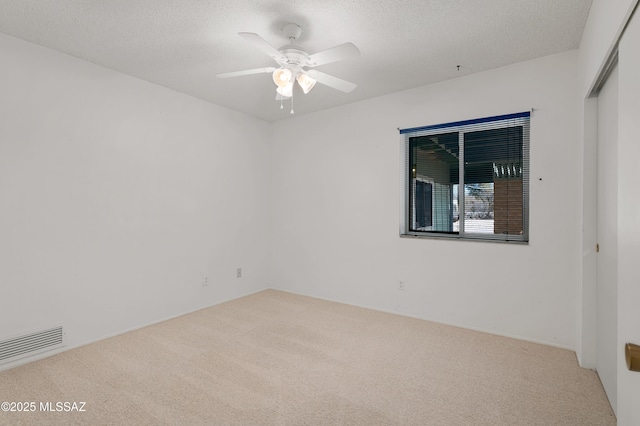 carpeted empty room featuring a ceiling fan, visible vents, and a textured ceiling