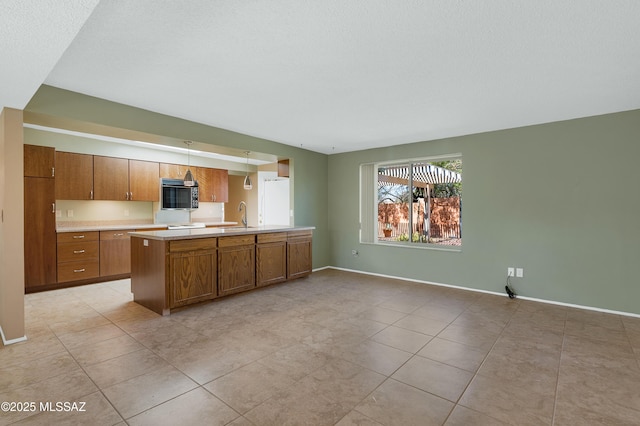 kitchen featuring a sink, stainless steel microwave, brown cabinetry, light countertops, and baseboards