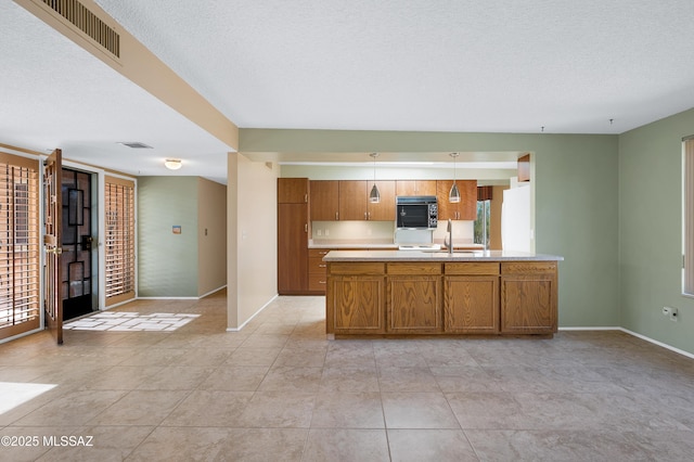 kitchen with stainless steel microwave, visible vents, light countertops, brown cabinets, and a sink