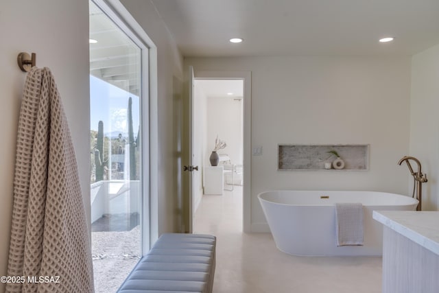 bathroom with recessed lighting, a freestanding tub, and concrete floors