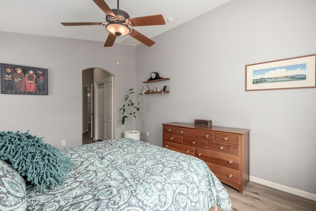 bedroom with light wood-style floors, baseboards, arched walkways, and ceiling fan