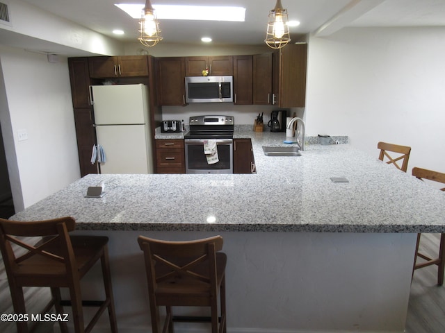 kitchen with a peninsula, a sink, visible vents, a kitchen breakfast bar, and appliances with stainless steel finishes