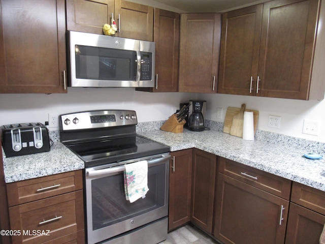 kitchen featuring stainless steel appliances, light wood-style flooring, and light stone countertops