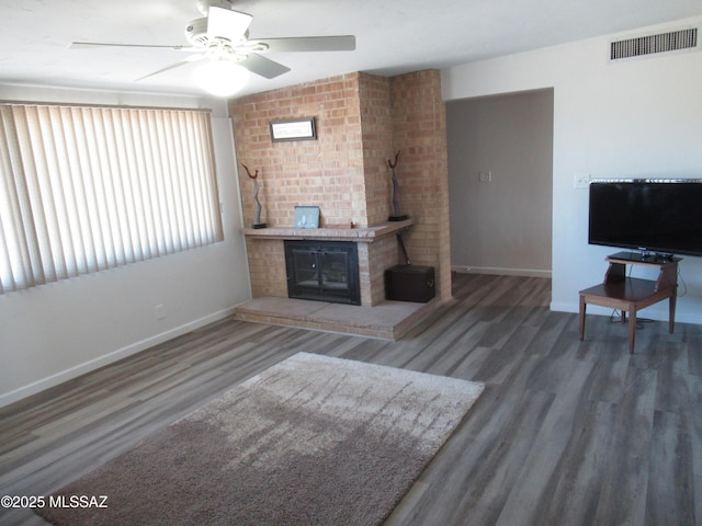 living room featuring a brick fireplace, wood finished floors, visible vents, and baseboards