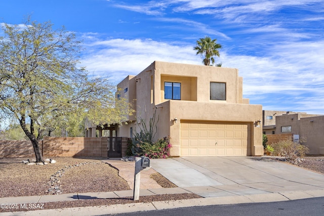 pueblo revival-style home featuring concrete driveway, fence, and stucco siding