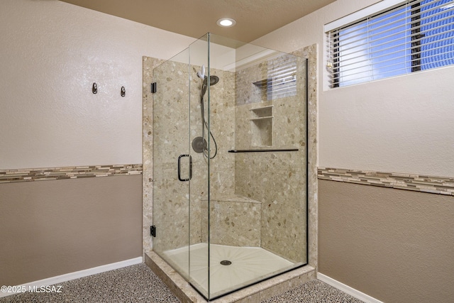 full bath with a textured wall, a shower stall, and baseboards