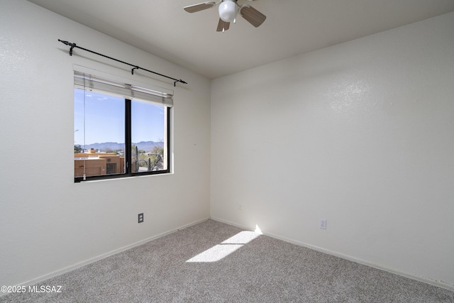 carpeted empty room with ceiling fan, a mountain view, and baseboards