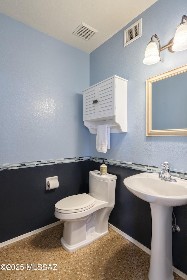 half bath with toilet, baseboards, and visible vents