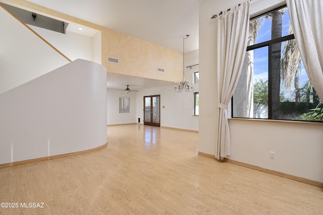 unfurnished living room featuring baseboards, visible vents, wood finished floors, a high ceiling, and ceiling fan with notable chandelier