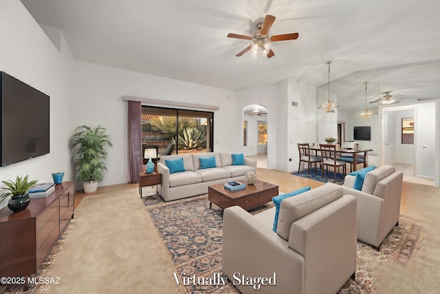 living area with lofted ceiling, arched walkways, a ceiling fan, and light colored carpet