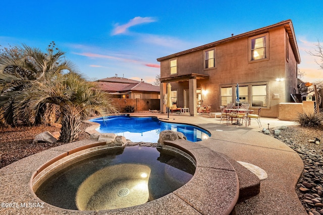 pool at dusk with a patio area, fence, a fenced in pool, and an in ground hot tub