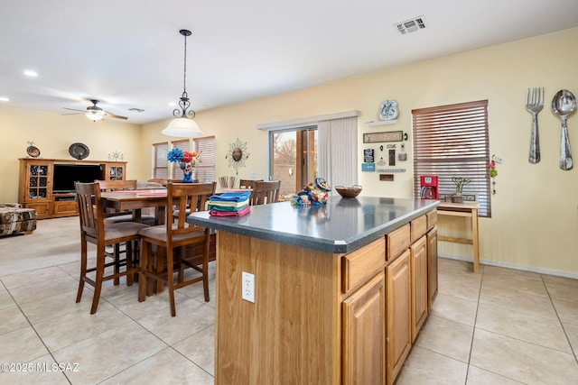 kitchen with light tile patterned flooring, a kitchen island, visible vents, dark countertops, and pendant lighting