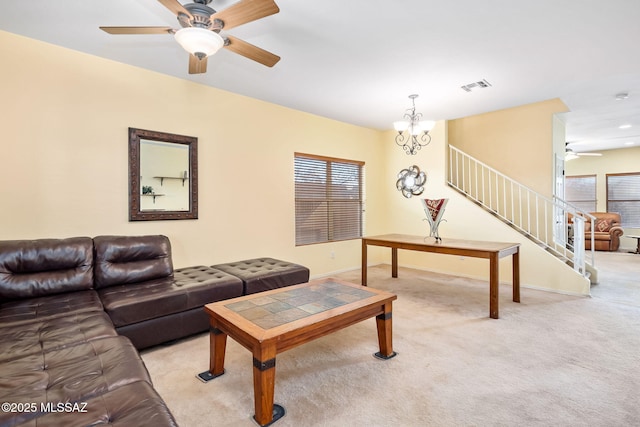 carpeted living room featuring ceiling fan with notable chandelier, stairway, visible vents, and baseboards