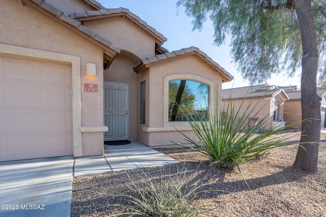 doorway to property featuring a garage, a tiled roof, and stucco siding