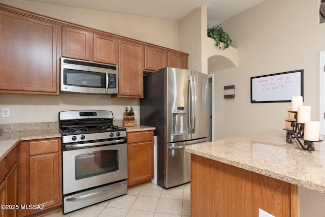 kitchen with light tile patterned floors, light stone counters, stainless steel appliances, and brown cabinetry