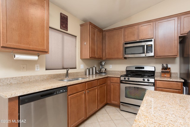 kitchen with brown cabinetry, lofted ceiling, appliances with stainless steel finishes, a sink, and light tile patterned flooring