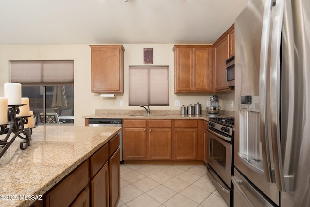 kitchen featuring light stone counters, brown cabinets, stainless steel appliances, a sink, and light tile patterned flooring