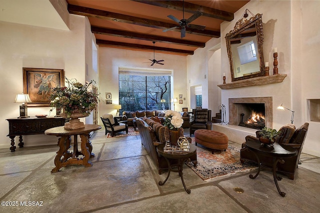 living area with beamed ceiling, a high ceiling, a premium fireplace, a ceiling fan, and concrete floors