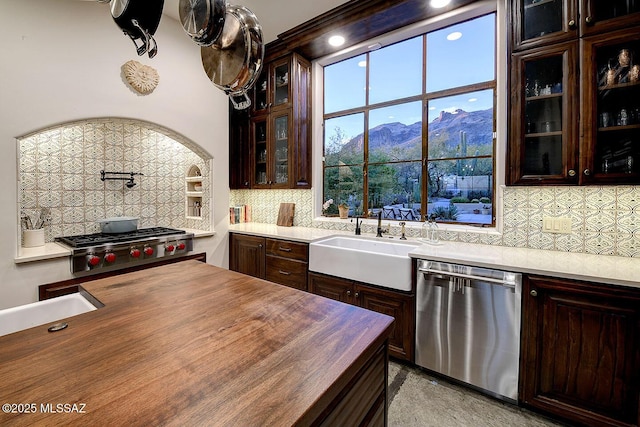 kitchen featuring decorative backsplash, stainless steel dishwasher, glass insert cabinets, a sink, and dark brown cabinets